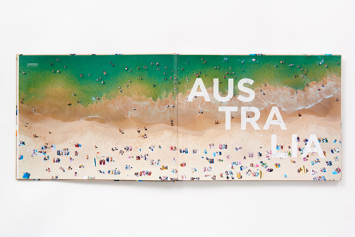 Open Beaches book displaying Gray Malin aerial beach photography of people swimming in turquoise water, with the large white text “AUSTRALIA” printed across the pages.