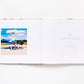 Open book from the Beaches collection featuring Gray Malin aerial photography of a person standing by a blue and white helicopter on the left page and the text “À LA PLAGE” on the right.