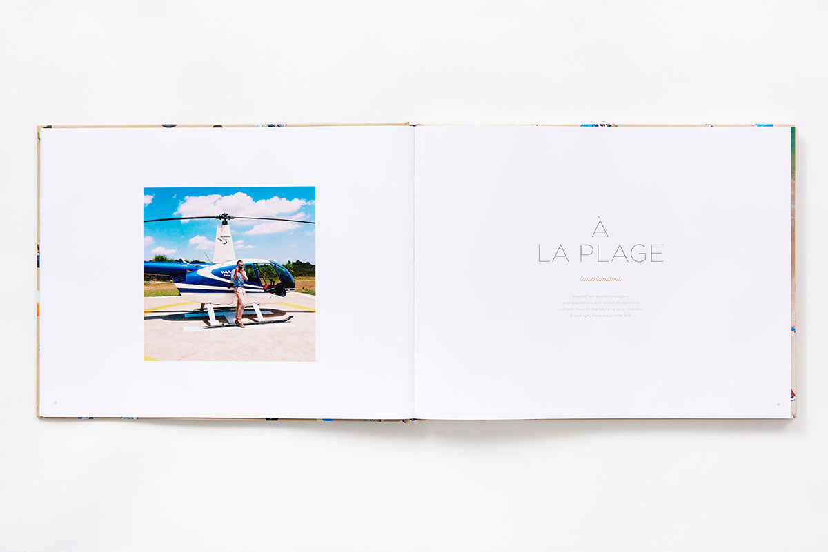 Open book from the Beaches collection featuring Gray Malin aerial photography of a person standing by a blue and white helicopter on the left page and the text “À LA PLAGE” on the right.