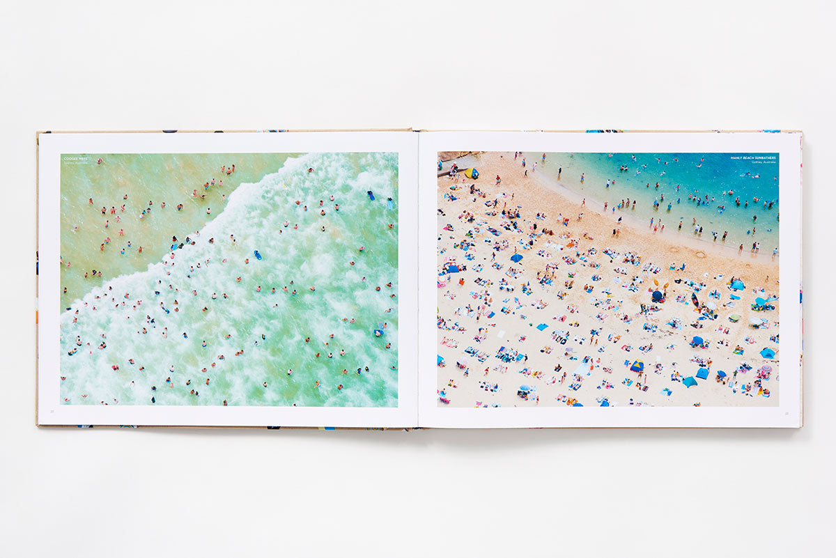 An open Beaches photography book by Gray Malin showing an aerial view of swimmers in ocean waves on the left page and sunbathers on a sandy beach on the right page.