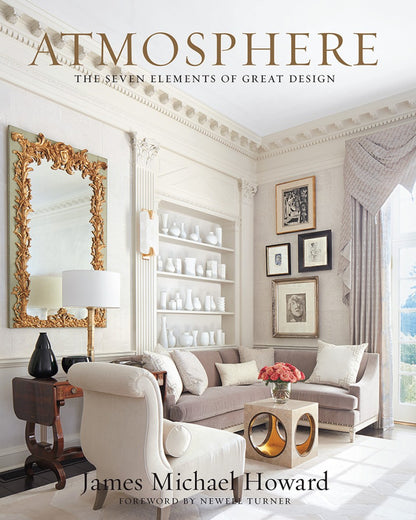 A formal living room featuring Atmosphere: The Seven Elements of Great Design, with a sofa, gallery wall of sketches, gold-framed mirror, and built-in shelves of white pottery.