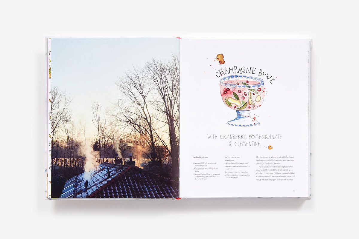 An open Home Made Christmas cookbook showing a photo of a snowy house at sunset on the left and a champagne bowl recipe with an illustration of the drink on the right.