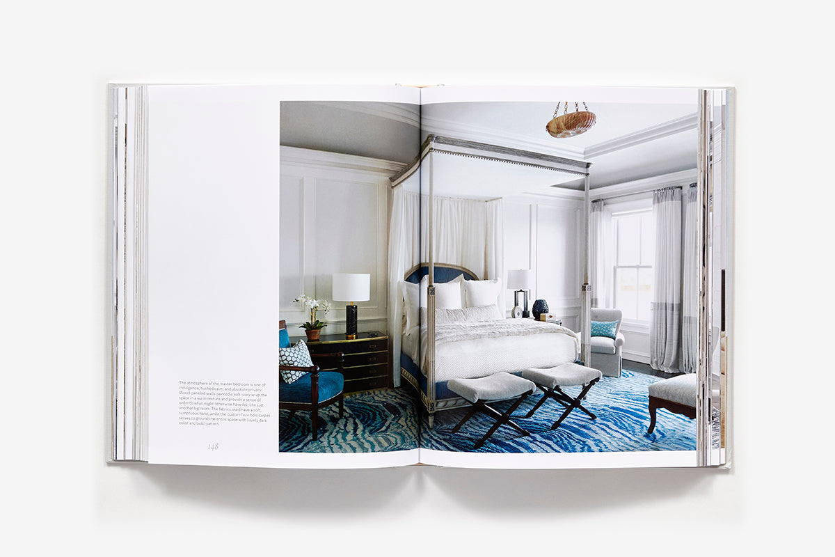 An open book of Atmosphere: The Seven Elements of Great Design displays a sophisticated bedroom interior with a canopy bed and a blue patterned carpet.