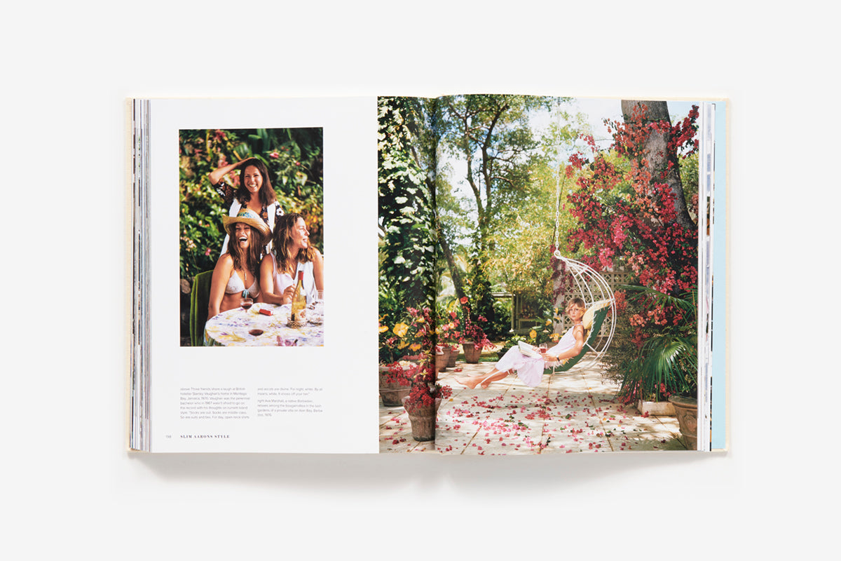 The book "Slim Aarons: Style" by Abrams features a captivating photo of three glamorous individuals at a table and a woman in a chic white dress on a hanging chair, surrounded by vibrant red flowers, epitomizing timeless fashion photography.