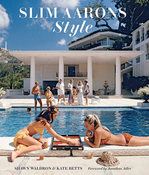 Two women in swimsuits play backgammon by a pool, capturing the essence of Slim Aarons' fashion photography. Glamorous personalities stand near a large white villa, perfectly embodying the allure on the cover of "Slim Aarons: Style" by Abrams.