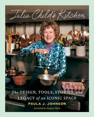 The book cover features a woman smiling while whisking in a copper-adorned kitchen, encapsulating the spirit of "Julia Child's Kitchen: The Design, Tools, and Stories" by Abrams. Home cooks will find it essential, with a foreword by Jacques Pépin linking past to present culinary practices.