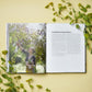 On a yellow surface adorned with green leafy sprigs lies A Year in Flowers by Chronicle Books, open to a spread that inspires creativity: the left page features an image of a woman gathering blossoms—an ideal scene for envisioning seasonal arrangements—while the right page, titled “Fundamental Ingredients,” provides essential guidance on bouquet design and flower care.
