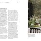 A formal dining table set with white linens and floral centerpieces sits in front of a fireplace and a large nature mural, beautifully capturing the exquisite interior design featured in “Moments At Home” by Chronicle Books. Text content appears on the left side of the image.