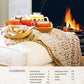 A cozy fireside feast unfolds with a tray of tea and cookies on an ottoman draped in a knitted blanket. At the bottom, you can find "Comfort: A Winter Cookbook" by Common Ground offering warmth and comfort against the chill with its contents list and page numbers elegantly displayed.