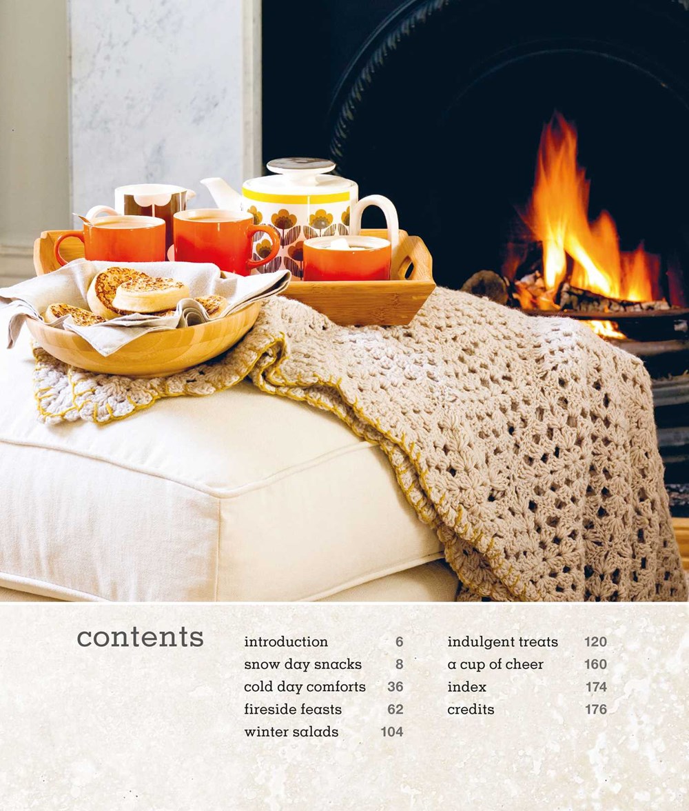 A cozy fireside feast unfolds with a tray of tea and cookies on an ottoman draped in a knitted blanket. At the bottom, you can find "Comfort: A Winter Cookbook" by Common Ground offering warmth and comfort against the chill with its contents list and page numbers elegantly displayed.