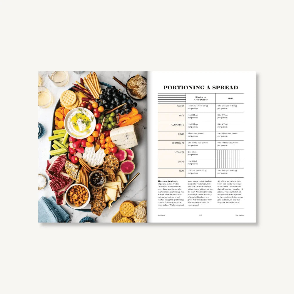 Open book of “Tables & Spreads” by Chronicle Books displaying a vibrant charcuterie board with assorted snacks on the left and a handy portioning guide table on the right, making it an ideal addition to any cookbook collection or food styling reference.
