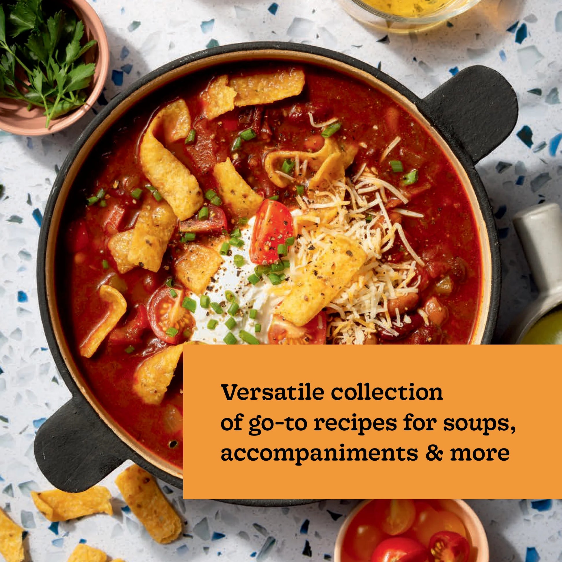 A bowl of chili topped with sour cream, shredded cheese, chives, and corn chips sits beside a garnish of chopped parsley, accompanied by text about Every Season Is Soup Season—a soup cookbook recipe collection from Chronicle Books featuring delicious and healthy soups.