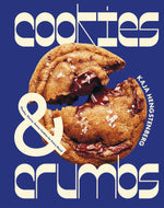 A large chocolate chip cookie broken in half sits on a blue background with the text “Cookies & Crumbs” and “Chronicle Books” displayed in bold, stylized fonts—perfectly capturing the irresistible appeal of gluten-free cookies.