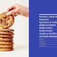 A hand holds a chocolate chip cookie above a stack of five cookies next to the blue table of contents from Cookies & Crumbs by Chronicle Books, highlighting delicious baking cookies and tempting gluten-free recipes.