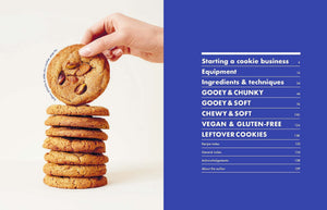 A hand holds a chocolate chip cookie above a stack of five cookies next to the blue table of contents from Cookies & Crumbs by Chronicle Books, highlighting delicious baking cookies and tempting gluten-free recipes.