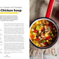 A saucepan filled with vibrant jerk chicken soup—a nourishing recipe from *Seriously Good Soups* by Chronicle Books—sits on a rustic table beside a cloth napkin, with the recipe text displayed on the left.