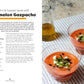 Two glasses of watermelon gazpacho topped with feta, mint, and seeds sit on a cloth beside a glass bottle of oil, while the left page from Seriously Good Soups by Chronicle Books features a recipe and description for this nourishing soup—a refreshing twist on comforting meal soups.