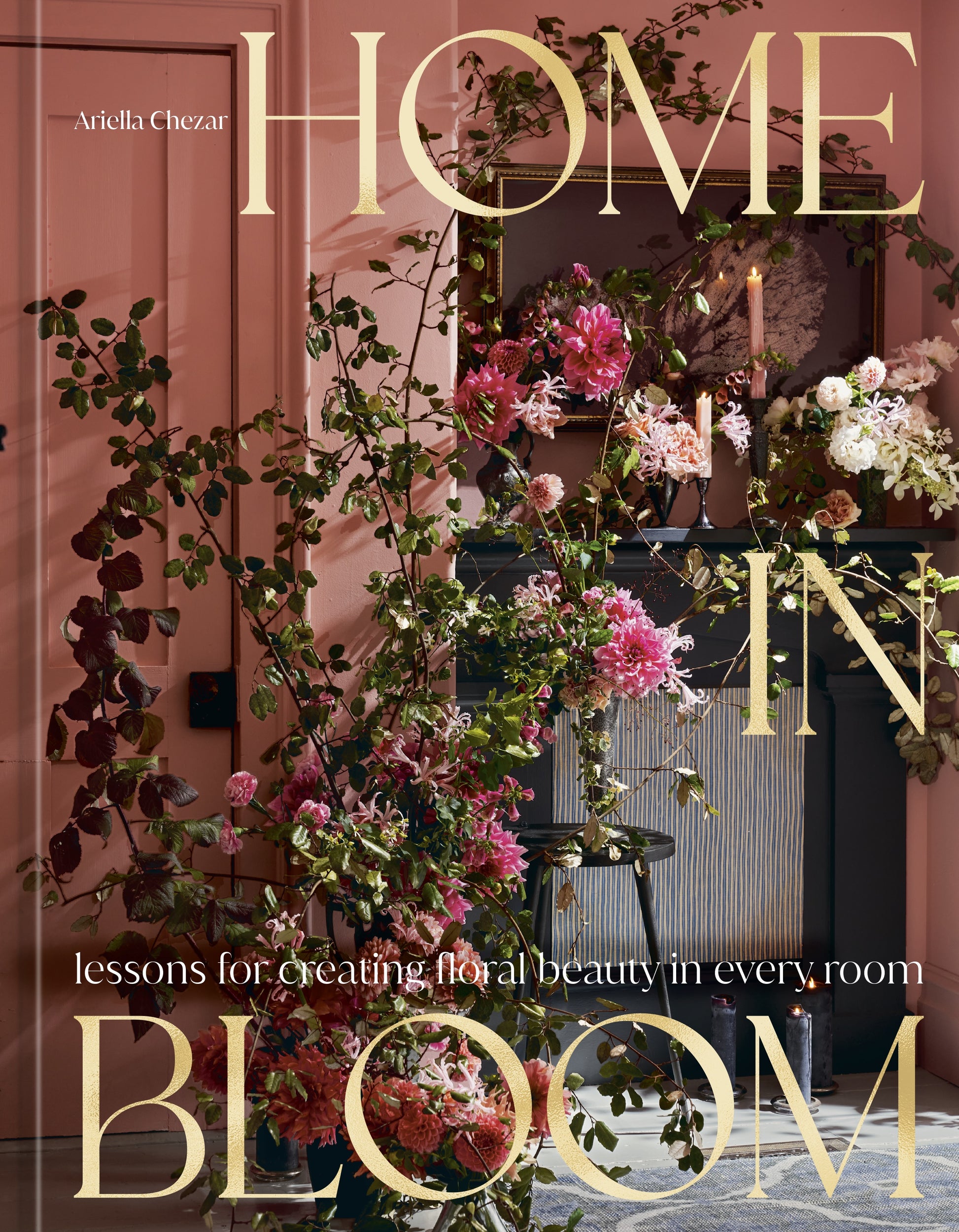 The cover of Home in Bloom by Penguin Random House features an elaborate floral arrangement displayed against a pink wall, with a candle and mirror in the background—an inspiring portrayal of flowers in interior design.