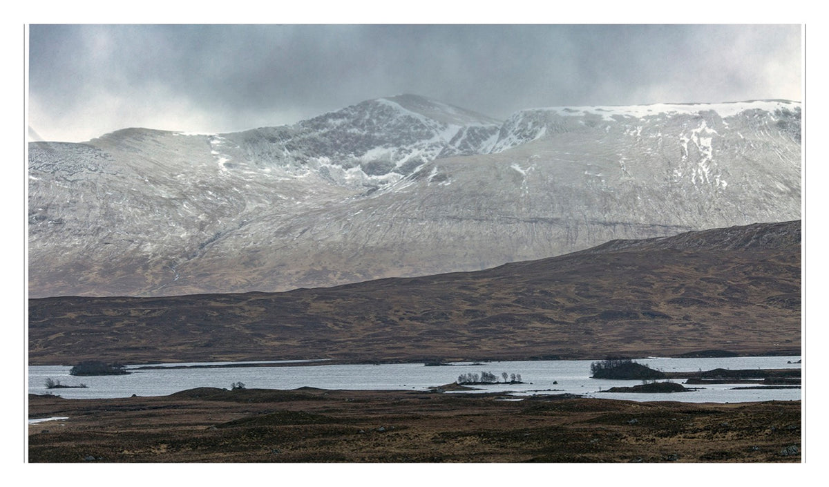 A wide, misty landscape with rolling hills, snow-dusted mountains in the distance, and a lake dotted with small islands evokes the tranquil beauty associated with historic Scottish settings—where celebrated single malt Scotch is made—just like those featured in “Scotch” from Penguin Random House.