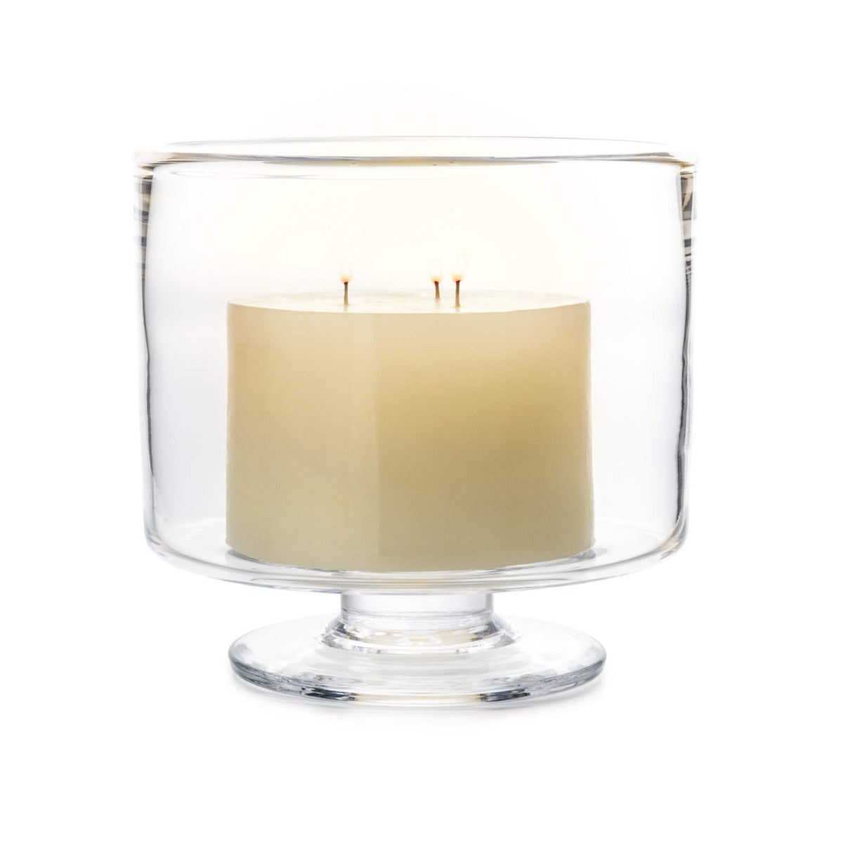 The Nantucket Hurricane Collection by Simon Pearce features a three-wick white candle in a clear glass holder with a short pedestal base, inspired by classic trifle dishes.