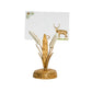 The Juliska Forest Walk Place Card Set features a gold and white decorative card holder shaped like a plant, supporting a card adorned with an enchanting watercolor stag illustration on grass—perfect for adding elegance to autumnal feasts or winter celebrations, all presented against a white background.