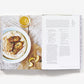 Open the book "The Saltwater Table: Recipes From The Coastal South" by Abrams to find a southern-style fish recipe alongside lemon slices and a glass of juice.