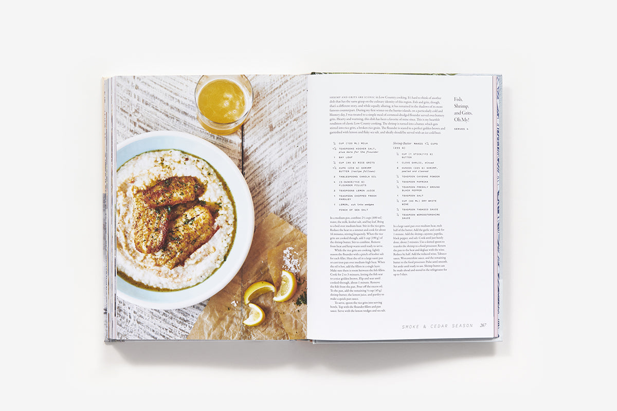 Open the book "The Saltwater Table: Recipes From The Coastal South" by Abrams to find a southern-style fish recipe alongside lemon slices and a glass of juice.