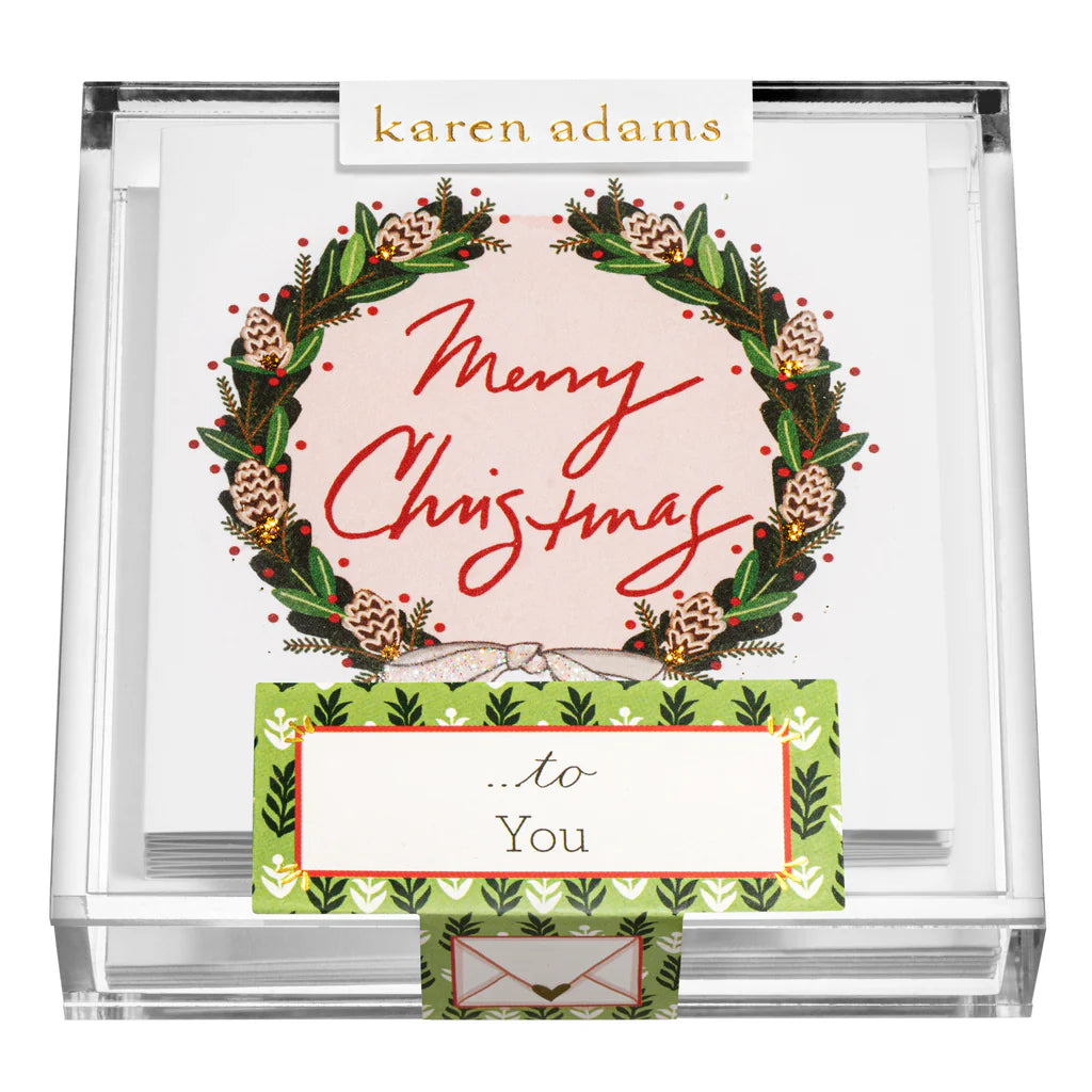 The Karen Adams Holiday Acrylic Gift Enclosures feature hand-glittered cards with a festive wreath and "Merry Christmas" on the front, labeled "...to You" and presented in a clear box—perfect for holiday gifting.