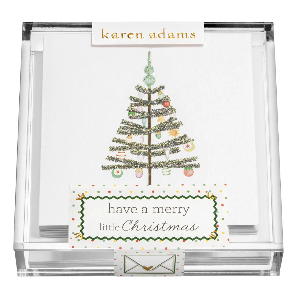 A clear box holds Karen Adams Holiday Acrylic Gift Enclosures—hand-glittered cards with decorated Christmas trees and “have a merry little Christmas”—perfect for adding sparkle to any holiday gift.