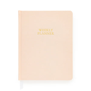 A closed, pale pink hardcover notebook from Sugar Paper, the Pale Pink Undated Weekly Planner features “WEEKLY PLANNER” in gold text on the cover. Designed to help you stay organized throughout the year, it includes a white ribbon bookmark extending from the bottom.