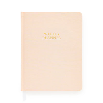 A closed, pale pink hardcover notebook from Sugar Paper, the Pale Pink Undated Weekly Planner features “WEEKLY PLANNER” in gold text on the cover. Designed to help you stay organized throughout the year, it includes a white ribbon bookmark extending from the bottom.