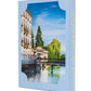A hardcover book titled Baur Au Lac: A Legacy by the Lake from Assouline, featuring a cover image of a riverside building, trees, and a bridge beneath a blue sky. Inspired by the timeless elegance of Zurich’s iconic luxury hotels, its spine is adorned with “BAUR AU LAC” in gold lettering.