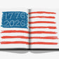 The open pages of America: The Imagination of a Nation by Assouline showcase a vibrant crayon illustration of the American flag, featuring “VOTE 2024” in the blue field—an evocative image that encapsulates the nation’s spirit as it nears its 250th anniversary, perfectly suited for an Assouline coffee table collection.