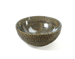 The Calaisio Round Bowl Collection features a round glass serving bowl with a woven crisscross pattern in brown and gold, inspired by traditional design and set against a white background.