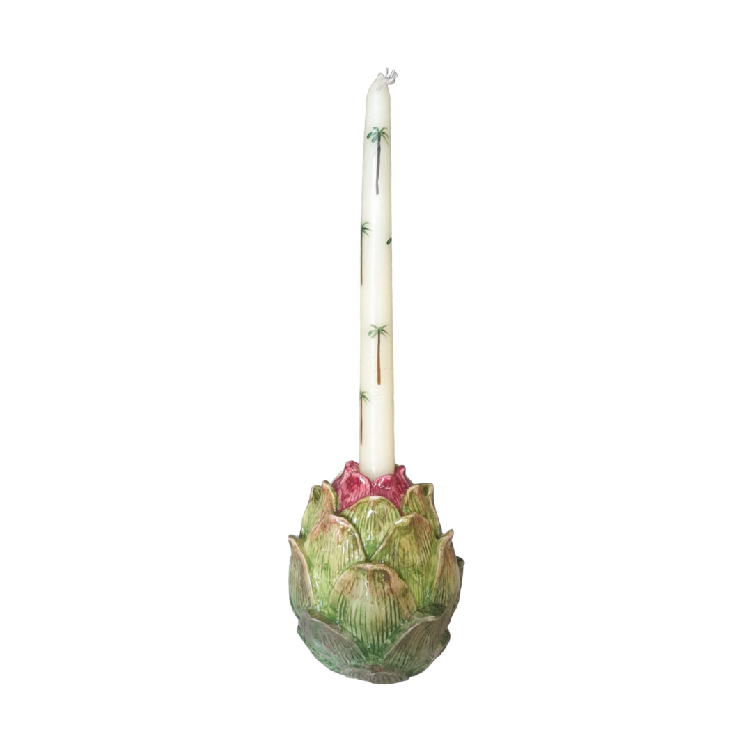 A white tapered candle with green palm tree motifs is set in a Les Ottomans Artichoke Decor and Serveware Collection holder, highlighting the allure of Italian hand-painted ceramics.