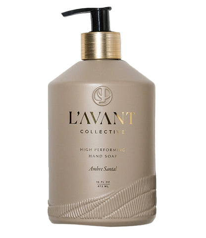 A 16 fl oz (473 ml) beige bottle of L'Avant Collective Ambre Santal Collection Hand Soap features a black pump, gold label, and a luxury blend of cardamom, amber, and cedar.
