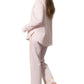 A person with long hair is wearing the Matouk Jasper Pajama Set in light pink cotton sateen with yellow piping, standing sideways and barefoot against a white background.