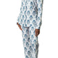 A person stands barefoot against a white background, wearing the Matouk Luca Pajama Set, a luxury long-sleeve, button-up set with a blue floral pattern crafted from Luca cotton percale.