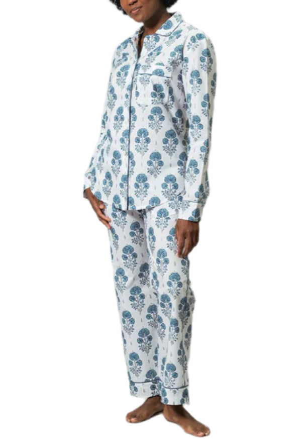 A person stands barefoot against a white background, wearing the Matouk Luca Pajama Set, a luxury long-sleeve, button-up set with a blue floral pattern crafted from Luca cotton percale.