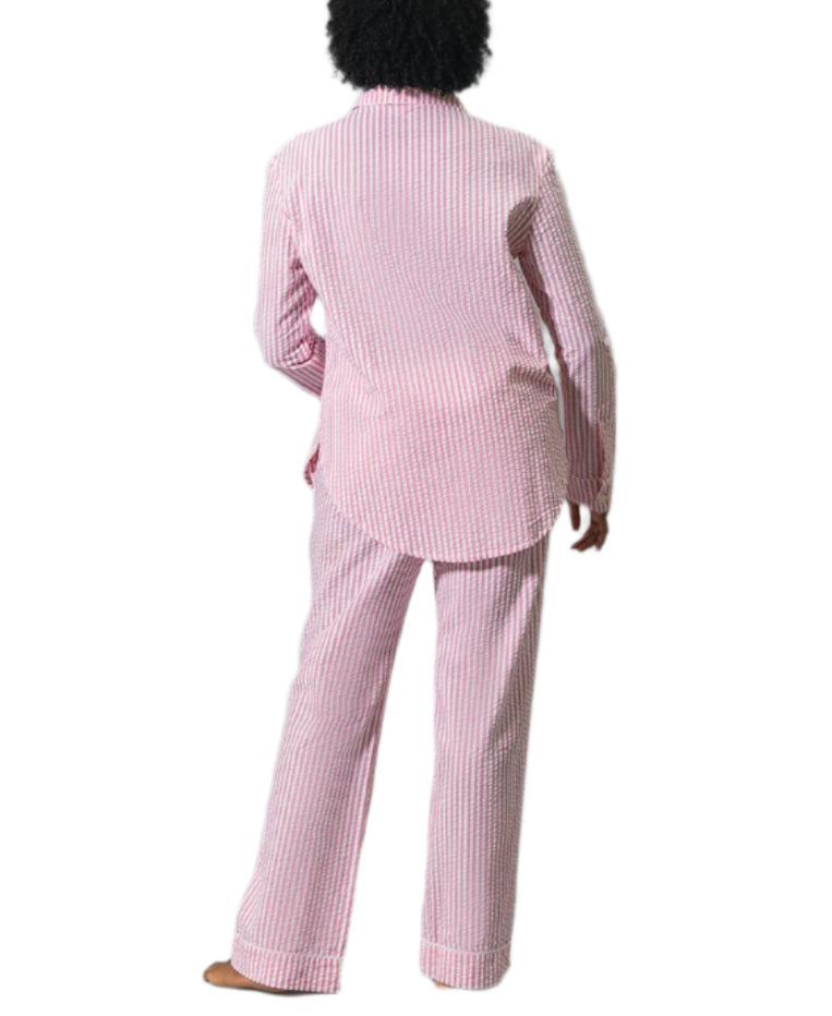 A person, seen from behind, wears the Matouk Matteo Pajama Set—a matching long-sleeve top and pants in pink-and-white classic stripes, crafted from soft seersucker cotton—set against a white background.