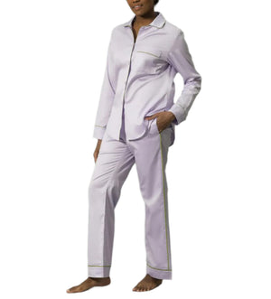 A person wears the Matouk Nocturne Pajama Set—a light-colored, long-sleeve, button-up leisurewear pajama set with matching pants—standing barefoot against a white background.