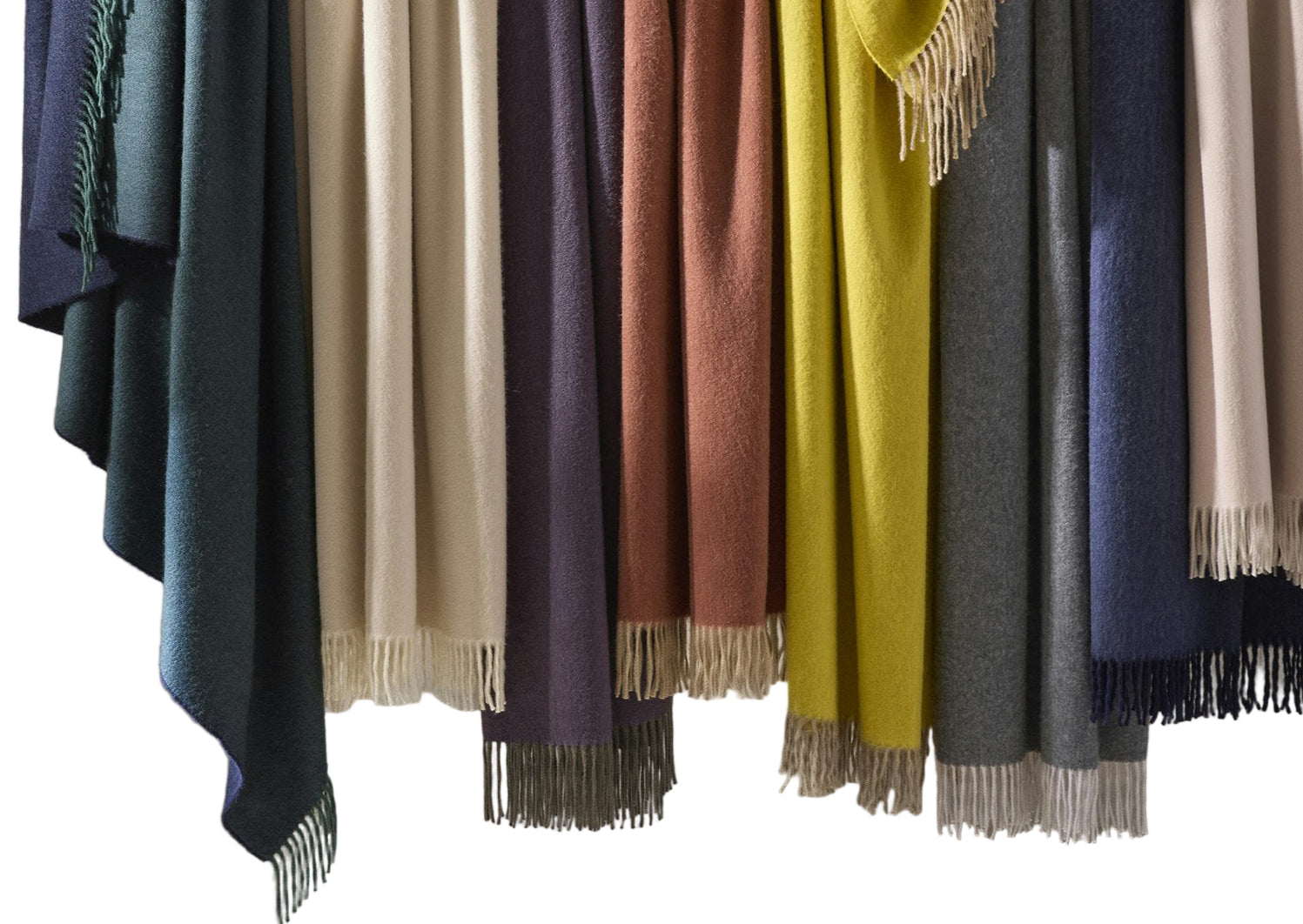 Matouk’s Paley Cashmere Throw, an oversized fringed blanket, is displayed side by side in green, beige, purple, rust, yellow, blue, and gray.