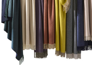 Matouk’s Paley Cashmere Throw, an oversized fringed blanket, is displayed side by side in green, beige, purple, rust, yellow, blue, and gray.
