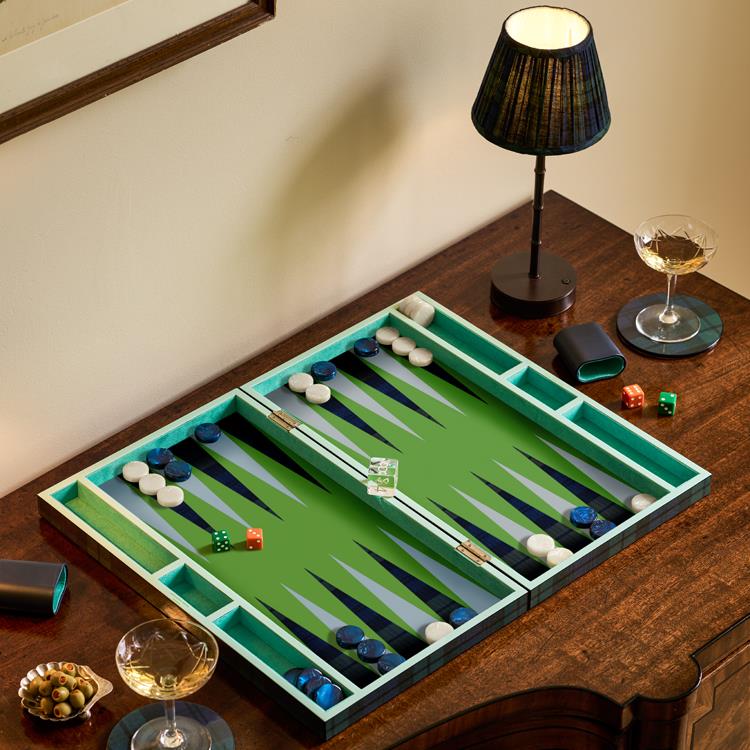 The Addison Ross Lacquer Backgammon Collection is displayed on a wooden table with glasses of wine, a bowl of olives, and a lamp.