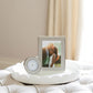 A framed photo and the Addison Ross Round Silver Alarm Clock rest on a white tray atop a cushioned surface, with soft curtains in the background—an inviting, cozy setup for your bedside table.