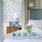 A bedroom with a blue and white floral theme, a bed with white linens, a wooden nightstand, framed photos, a floral lamp, and the Addison Ross Scalloped Pale Denim Lacquer Tray Collection holding mugs and flowers.