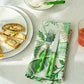 A plate with buttered bread, a green leaf napkin, and orange juice sits beside the colorful Addison Ross Wave Flatware Collection on a white tablecloth.