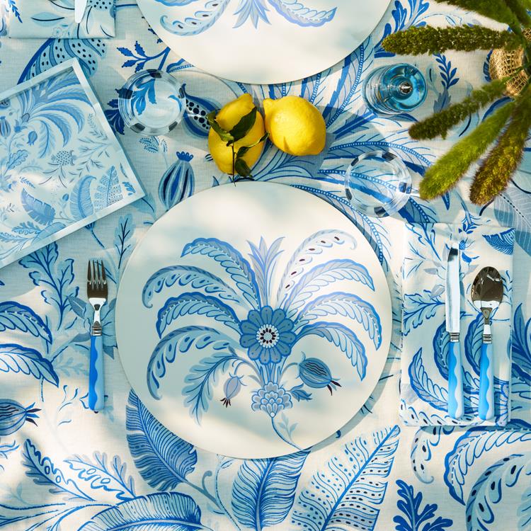 A table set with blue and white floral patterned plates, Addison Ross Wave Flatware Collection 16-piece set, glasses, napkins, a tablecloth, two lemons, and a green plant centerpiece.
