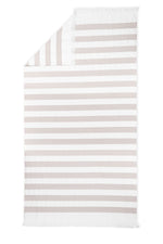 The Amado Beach Towel by Matouk features horizontal white and beige stripes, small fringes on the short edges, and a stylish folded corner—ideal for relaxing by the sea or pool.