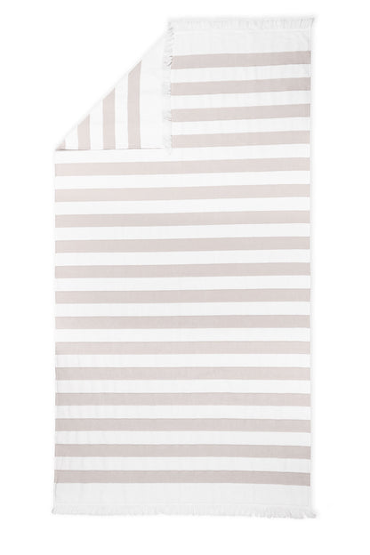 The Amado Beach Towel by Matouk features horizontal white and beige stripes, small fringes on the short edges, and a stylish folded corner—ideal for relaxing by the sea or pool.